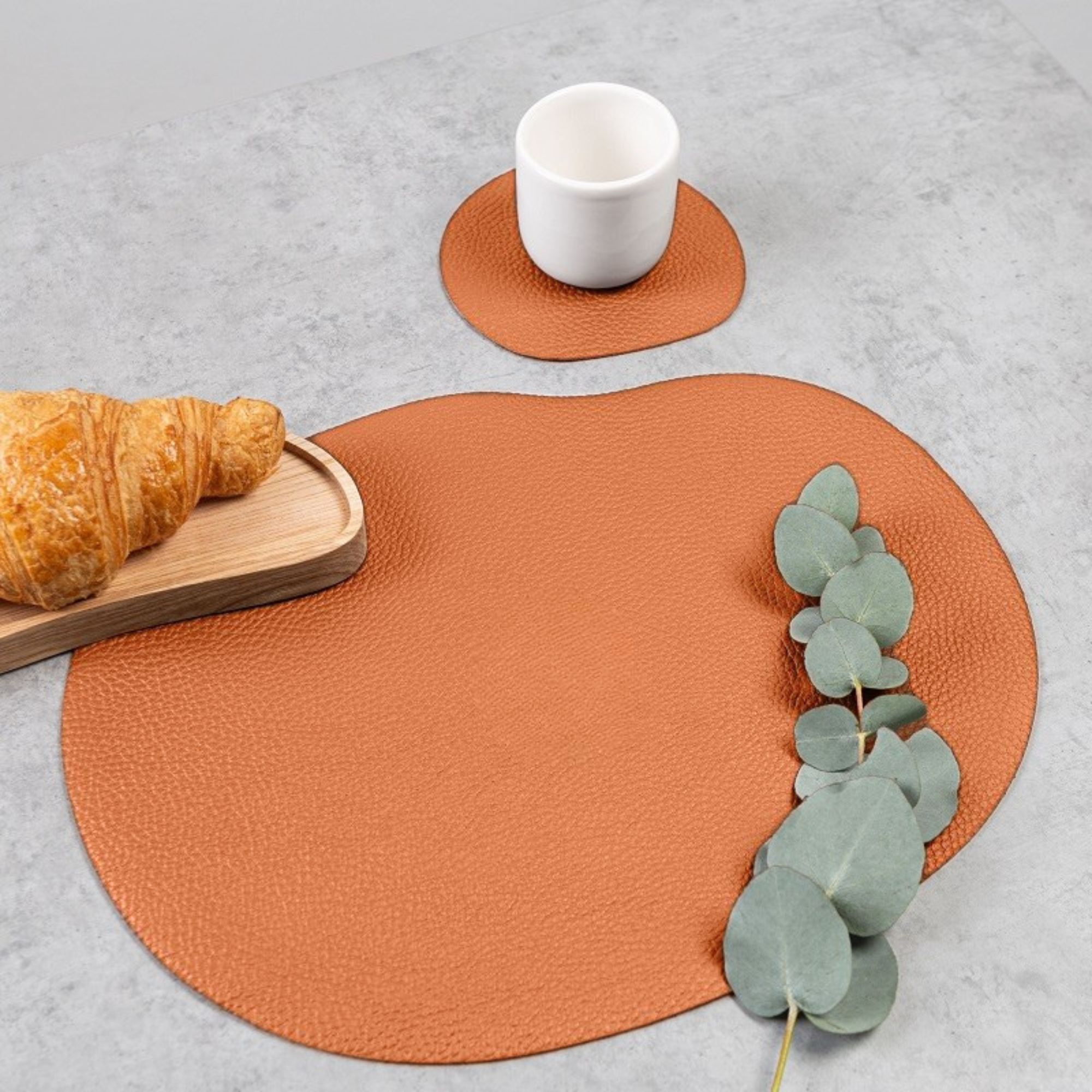 Mustard leather placemat and coaster with croissant on a table, highlighting the organic wavy shape.