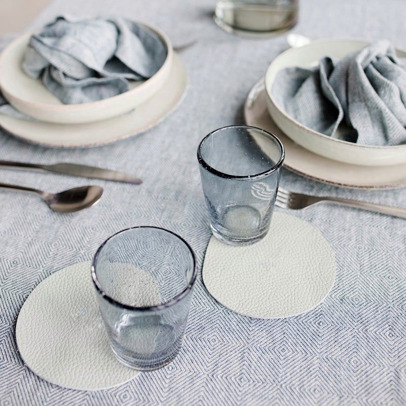 Light grey leather placemat and coaster on a dining table with elegant tableware and glassware.