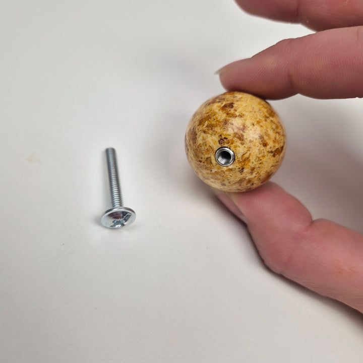 Round knob AMBER held in hand next to a metal screw for installation.