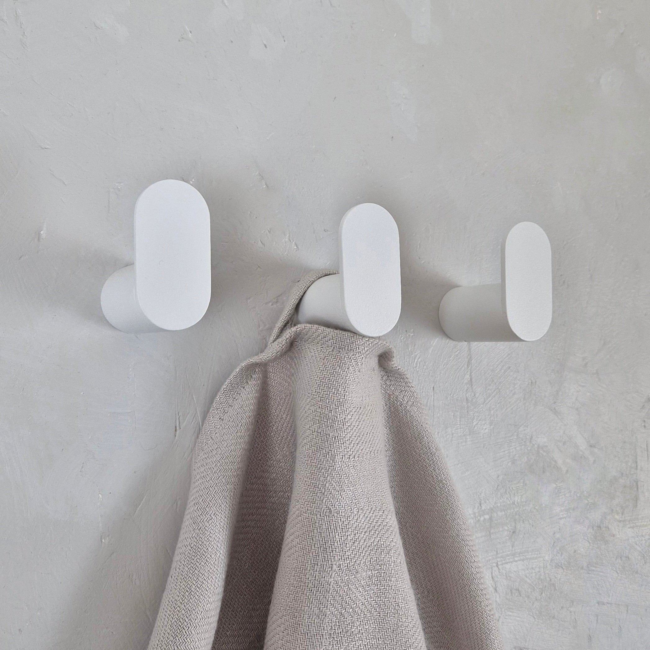 Minimalist wall hook in stylish white design, holding a soft blanket against a textured wall.