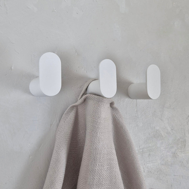 Minimalist wall hook in stylish white design, holding a soft blanket against a textured wall.