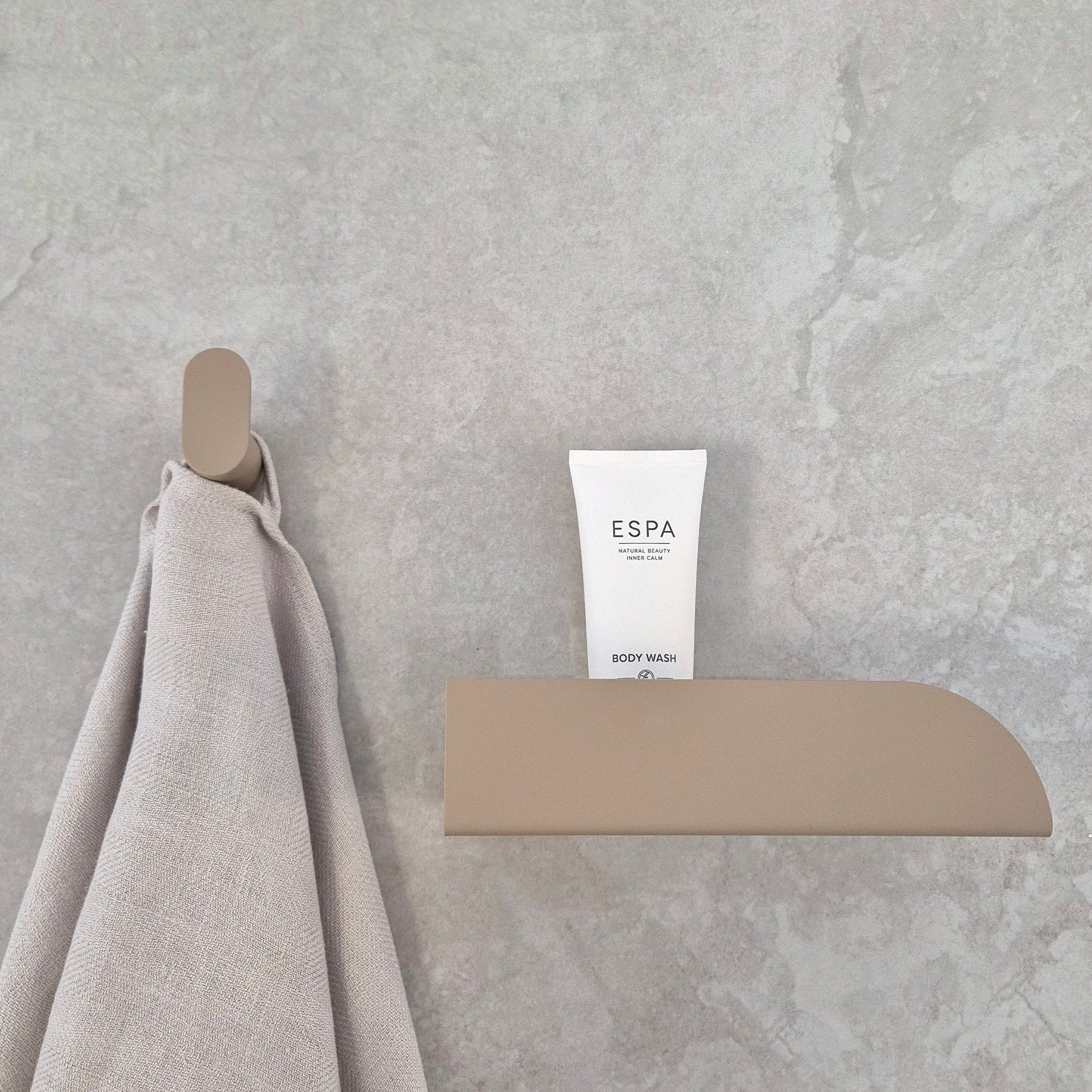 Minimalist wall hook with a towel and body wash tube on a bathroom wall