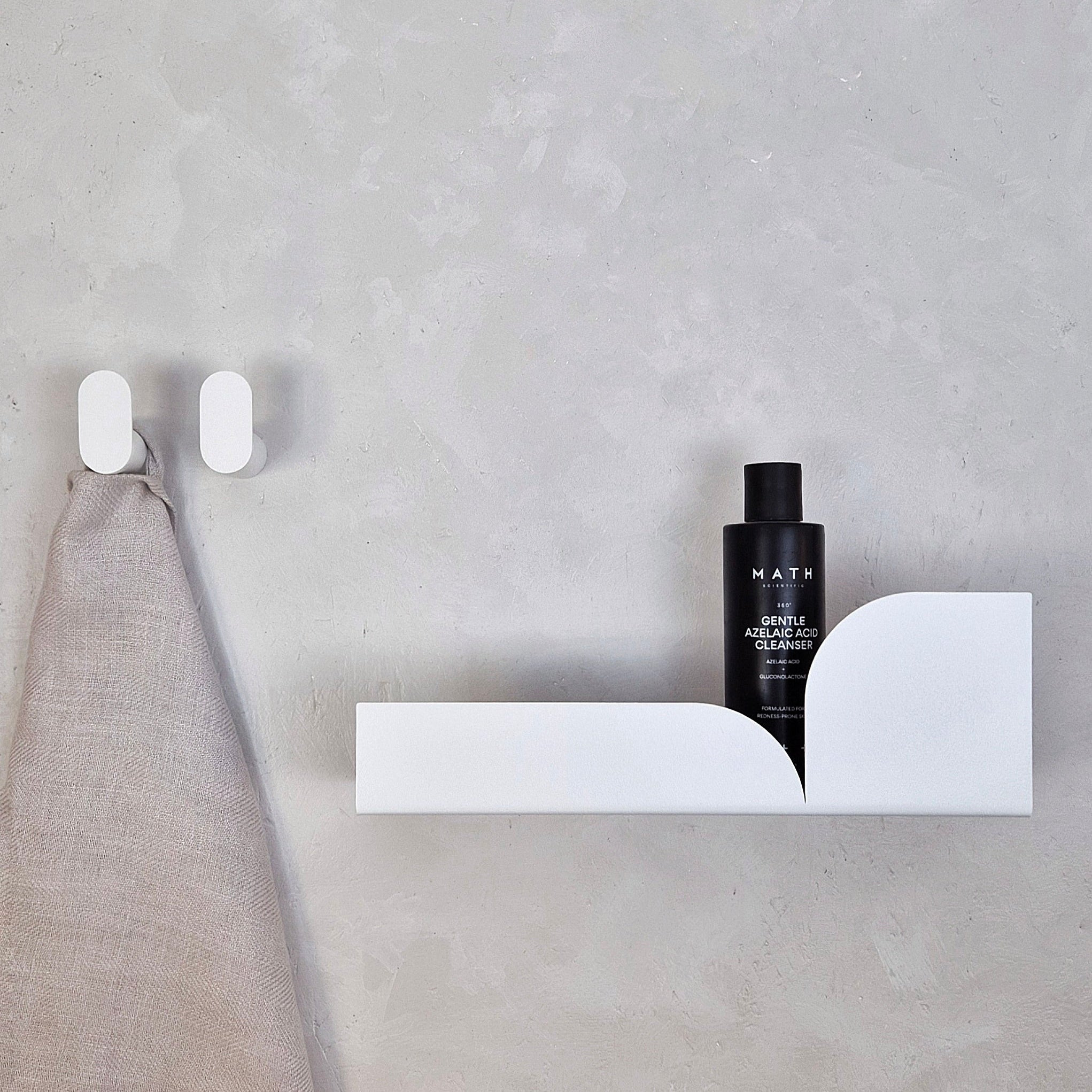 Minimalist wall hook BAUHAUS with sleek design holding a towel, complemented by a shelf and skincare bottle.
