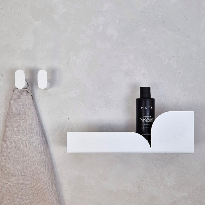 Minimalist wall hook BAUHAUS with sleek design holding a towel, complemented by a shelf and skincare bottle.