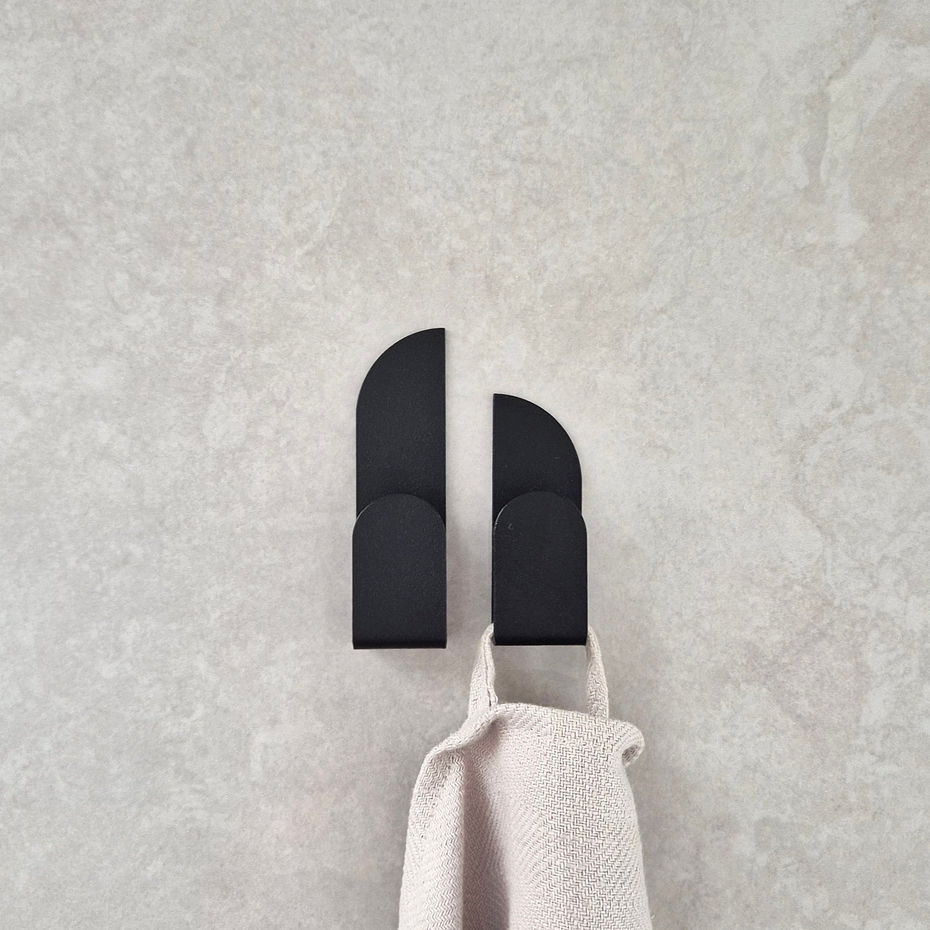 Adhesive wall hooks BAUHAUS holding a beige towel on a textured gray surface.