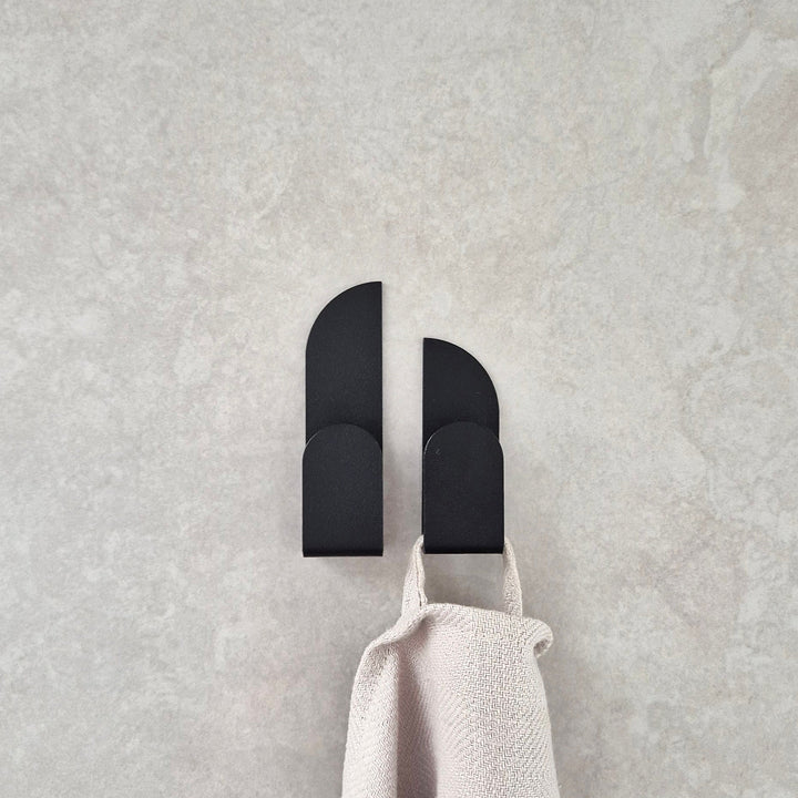 Adhesive wall hooks BAUHAUS holding a beige towel on a textured gray surface.