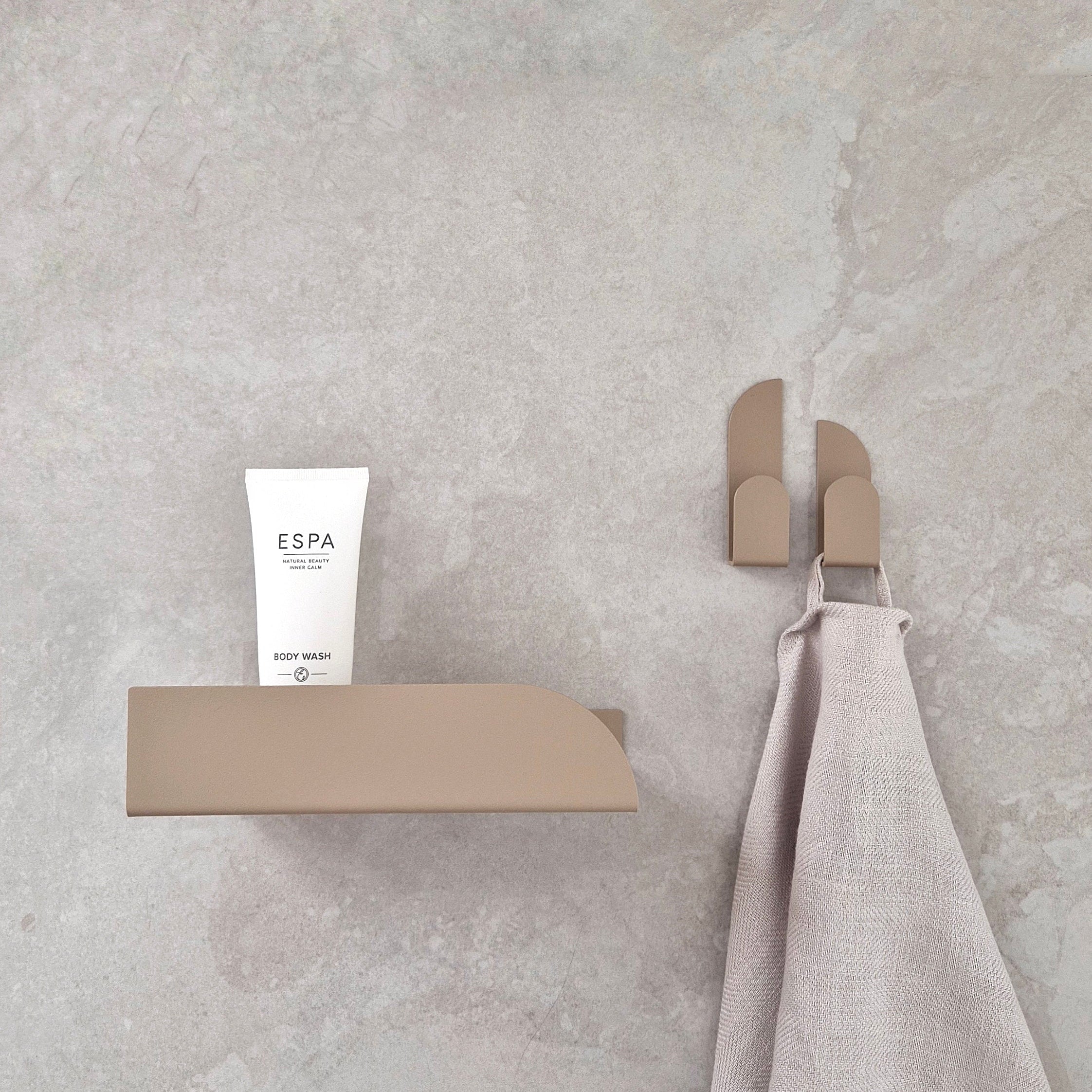 Adhesive wall hooks BAUHAUS holding a towel and a body wash product on a minimalist shelf.