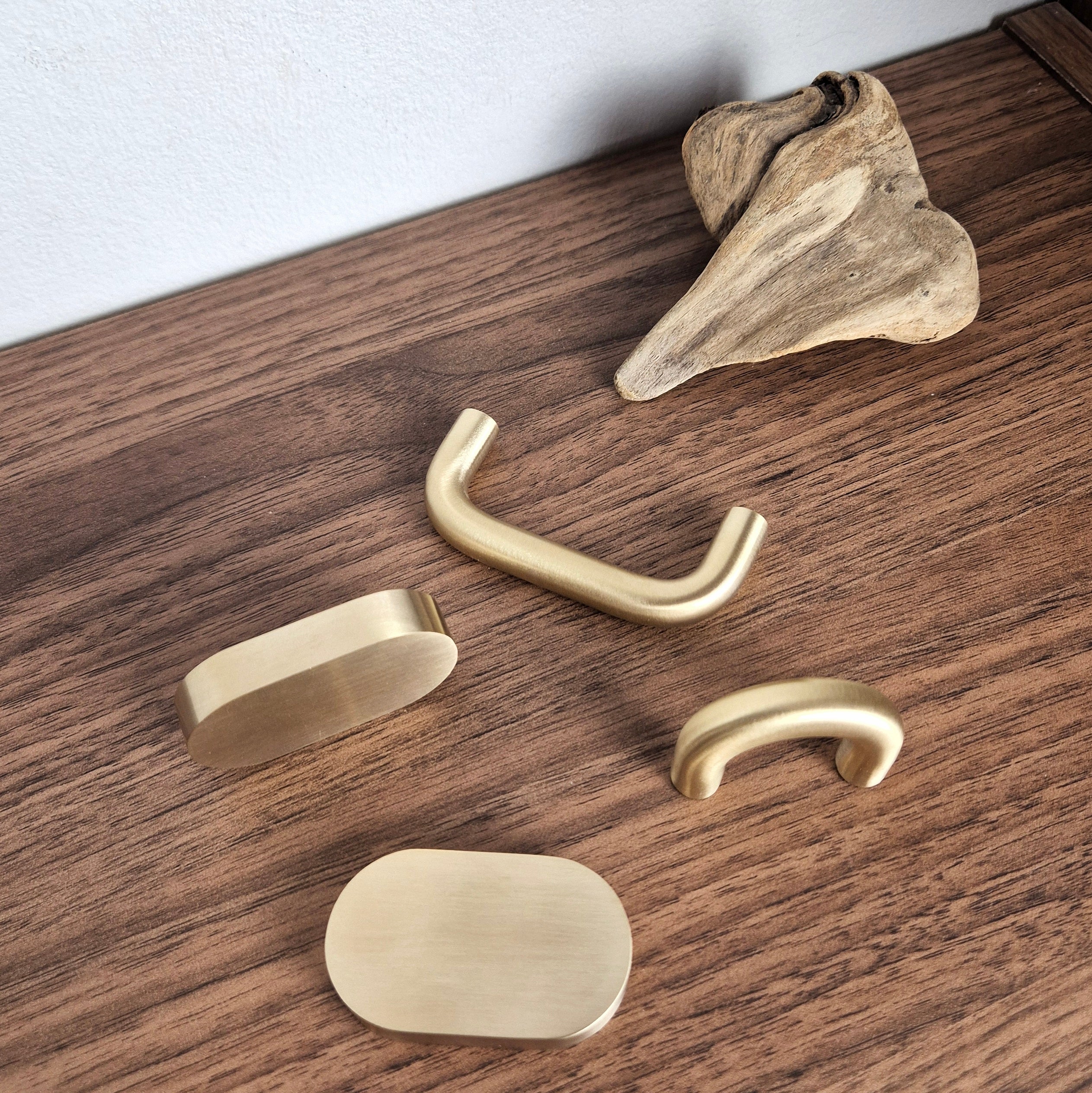 Four brass cabinet pulls arranged on a wooden surface, showcasing various designs in a warm satin finish.