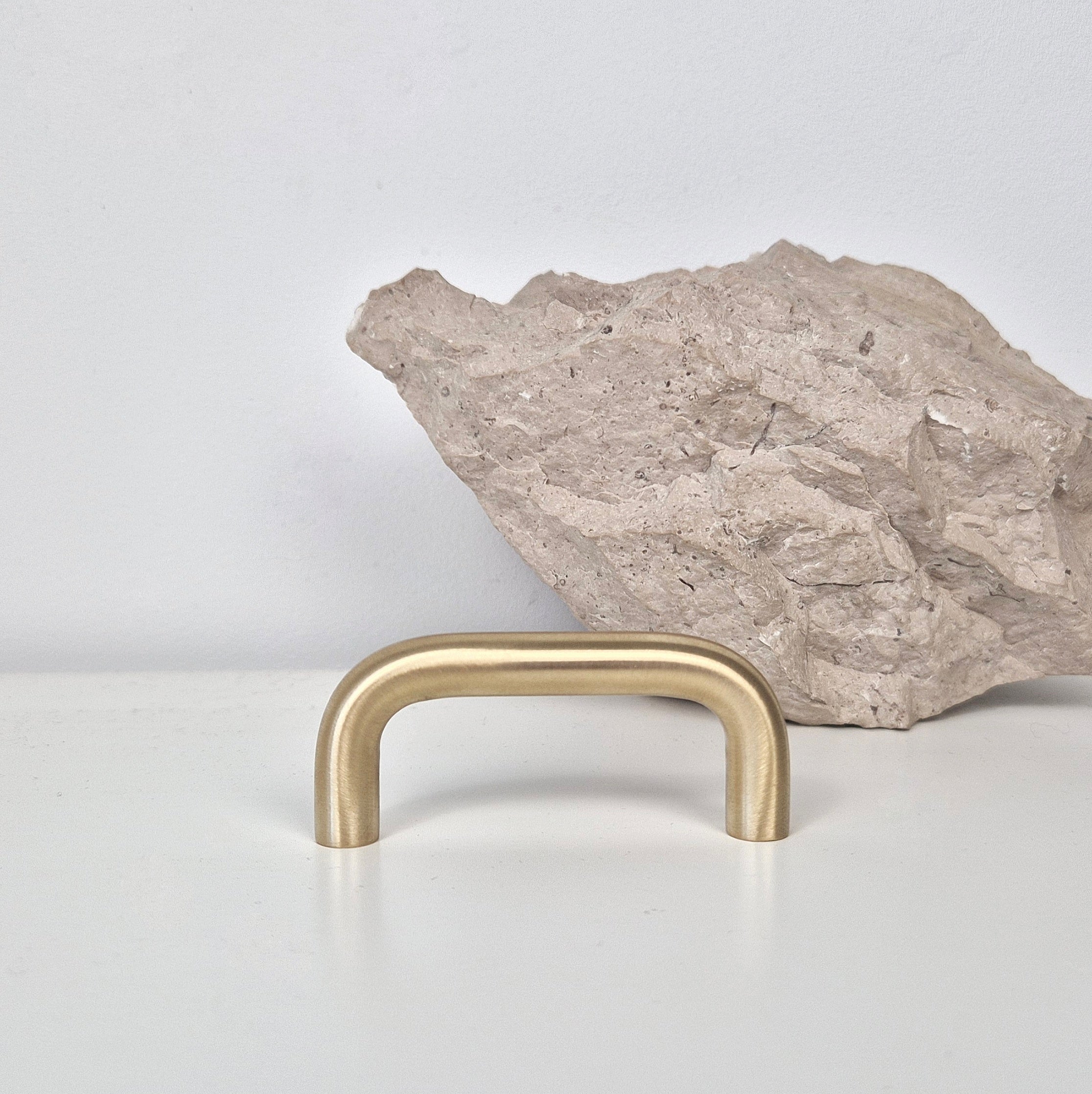 Brass cabinet pull DOME displayed in front of a textured rock on a white surface.
