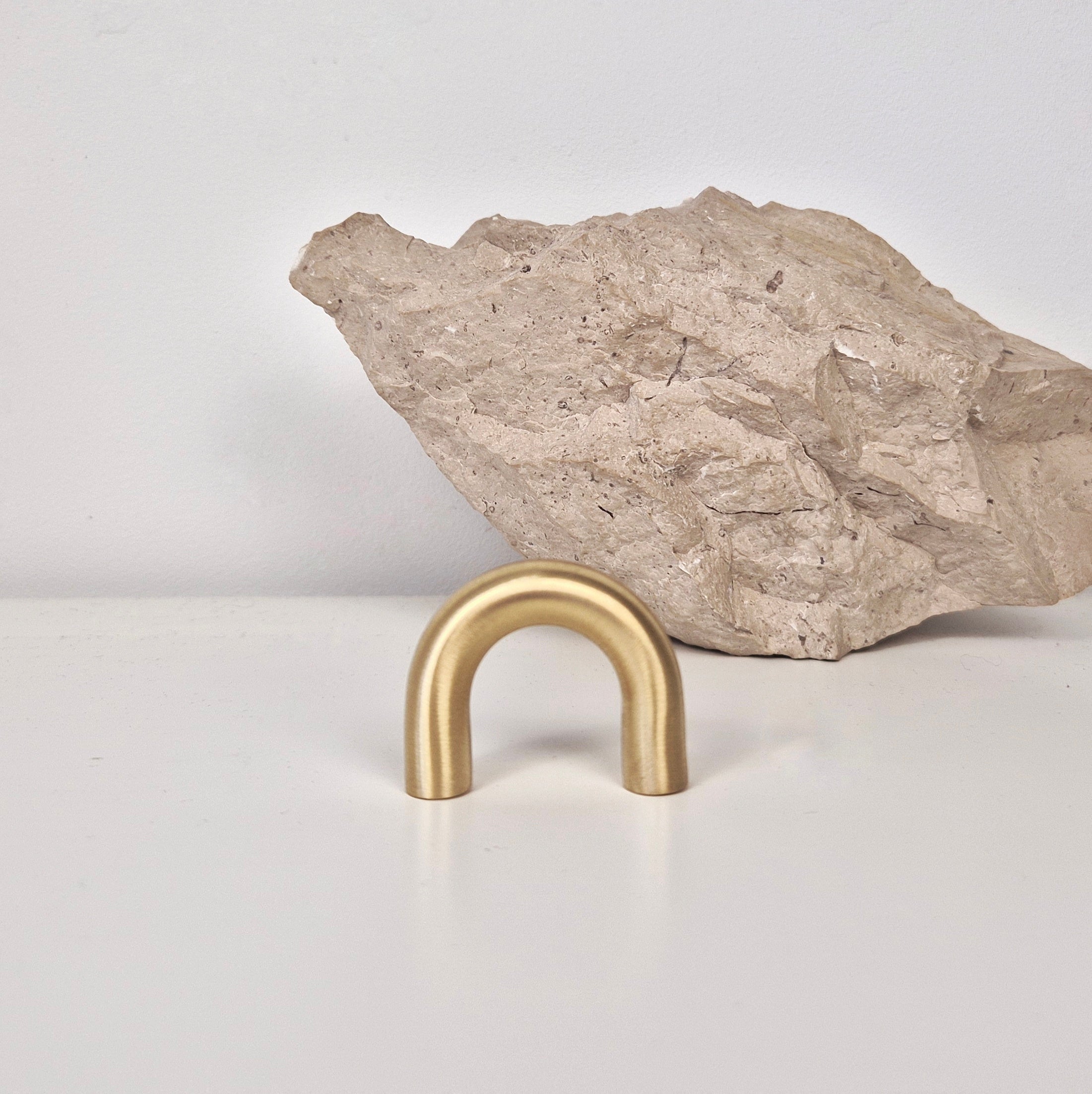 Brass cabinet pull DOME displayed in front of a decorative stone, showcasing its elegant satin finish.