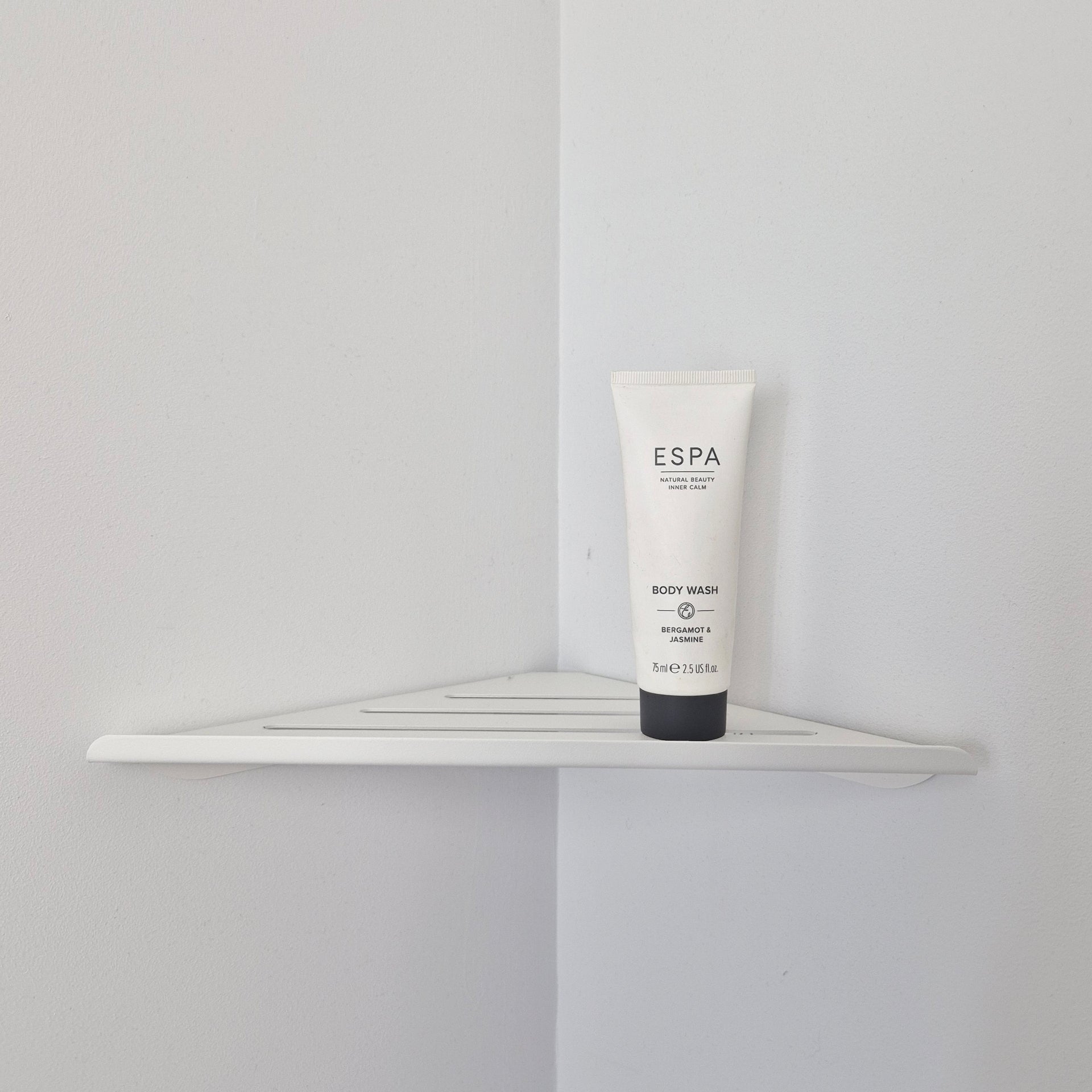 White shower corner shelf holding ESPA body wash on a minimalist design in a bright bathroom corner.