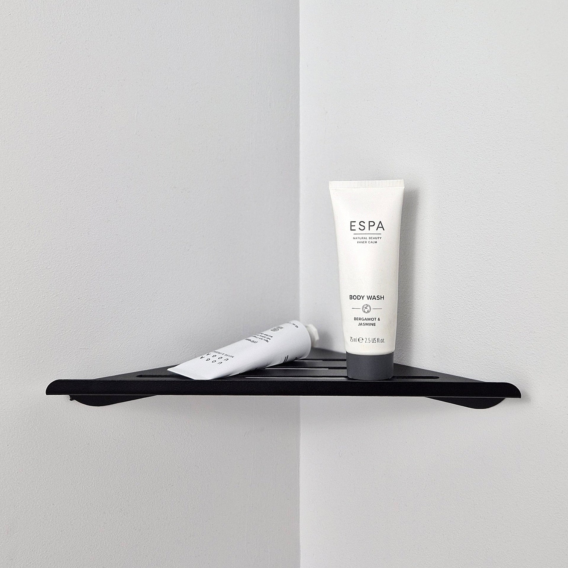 Black shower corner shelf holding body wash in a minimalist bathroom corner.