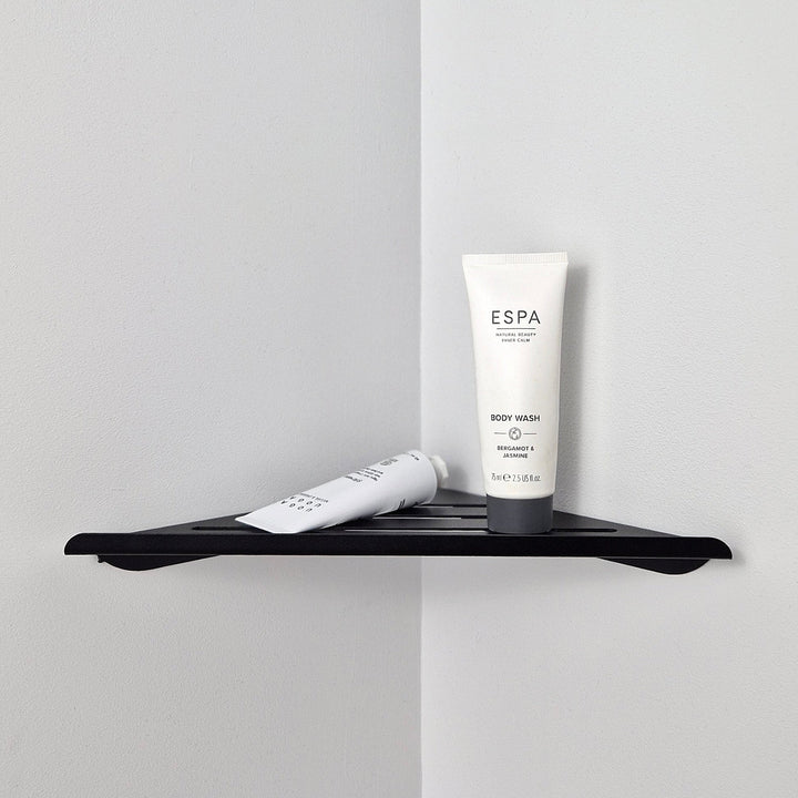 Black shower corner shelf holding body wash in a minimalist bathroom corner.
