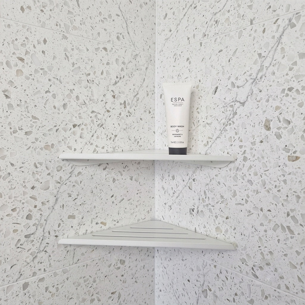 White shower corner shelf displaying body wash in a minimalist bathroom setting.