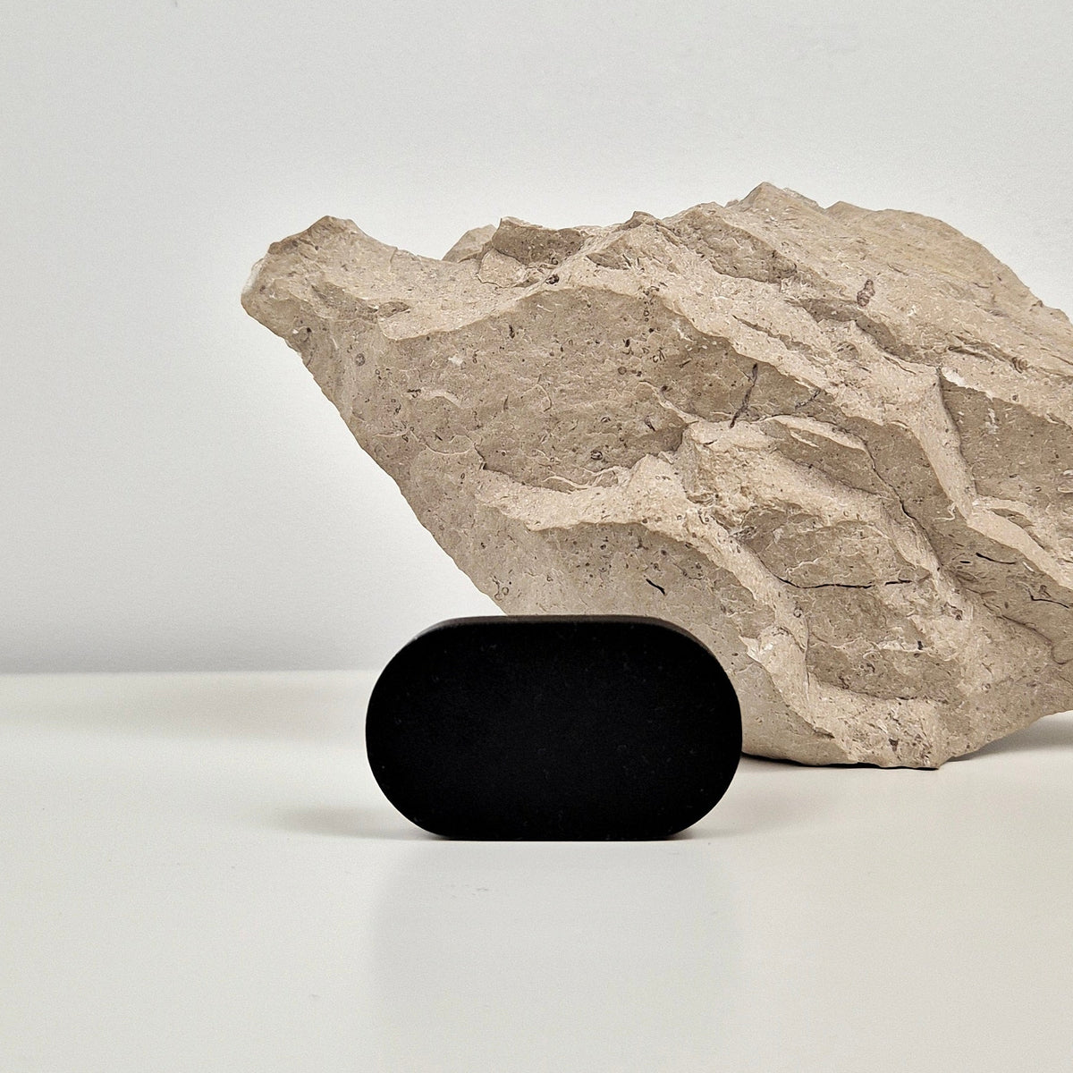 A small matte black oval handle standing on a white surface in front of a large textured beige rock against a light gray background.