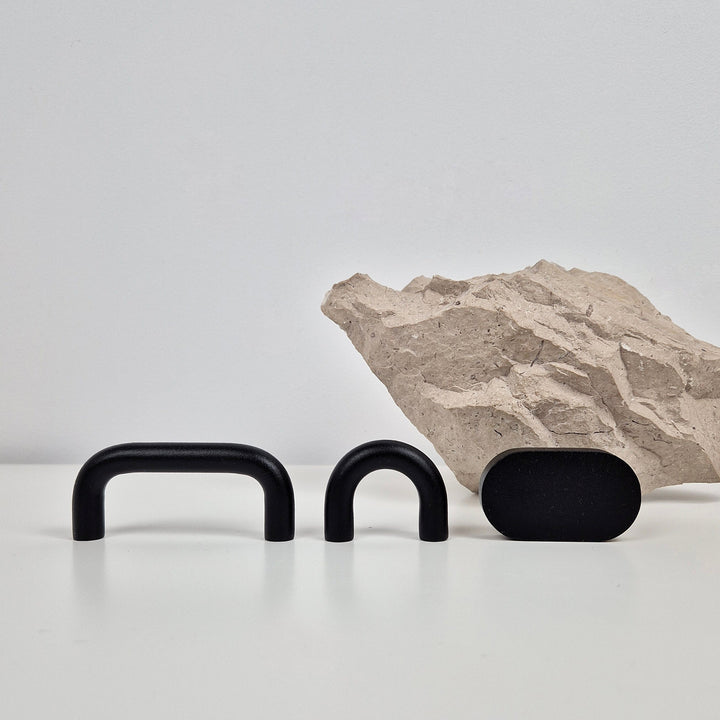 Three matte black hardware pieces, including two U-shaped handles and one oval knob, displayed on a white surface.