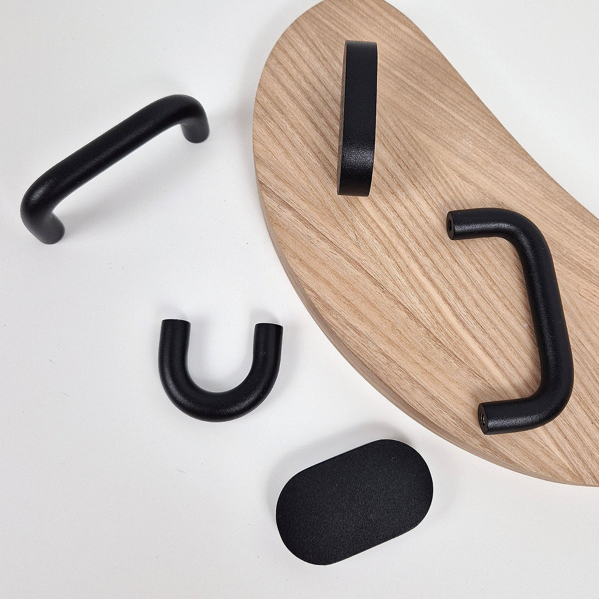 Matte black cabinet handles displayed on a light wood pegboard against a clean white background.