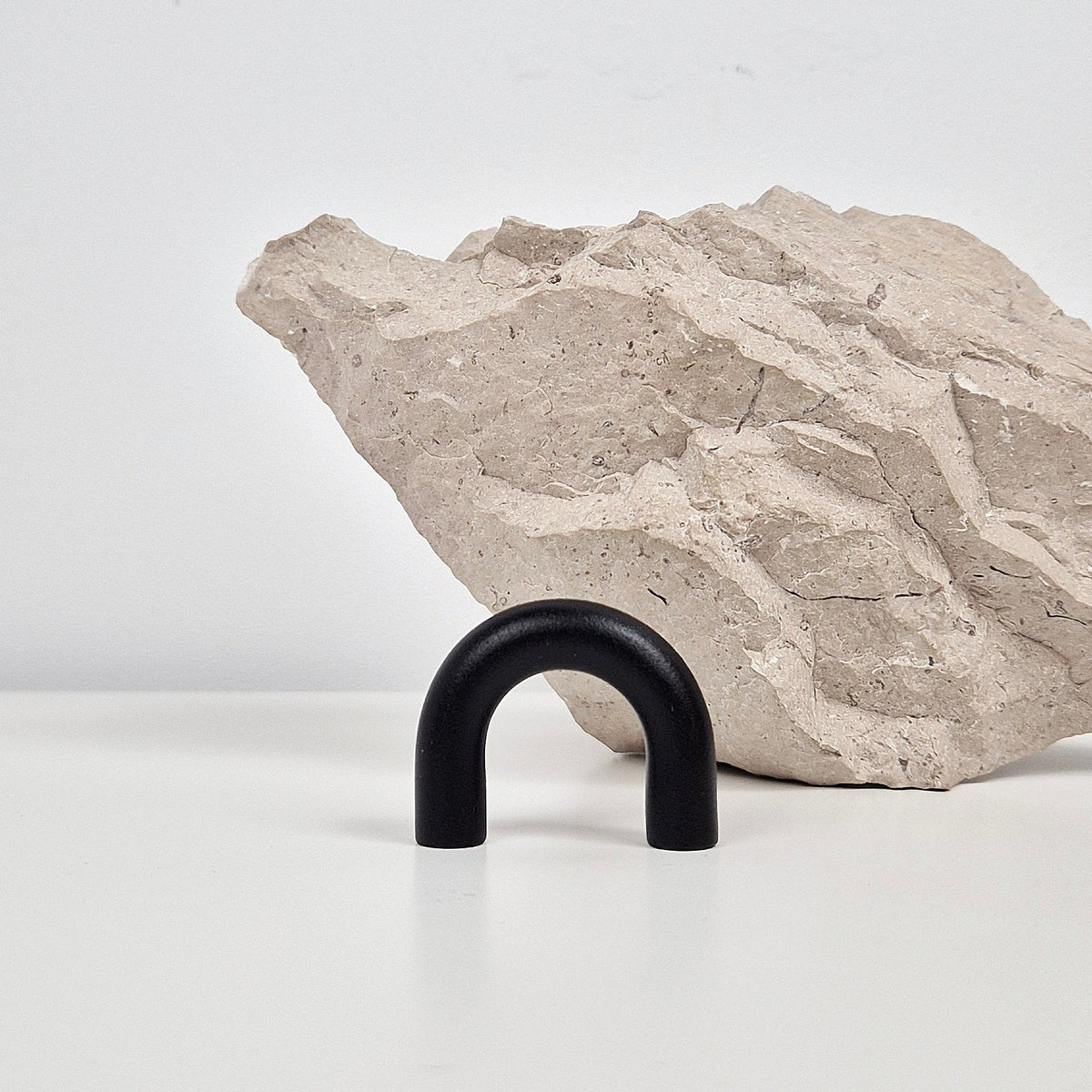A matte black U-shaped metal cabinet handle displayed on a white surface in front of a textured light beige stone prop against a clean white background.