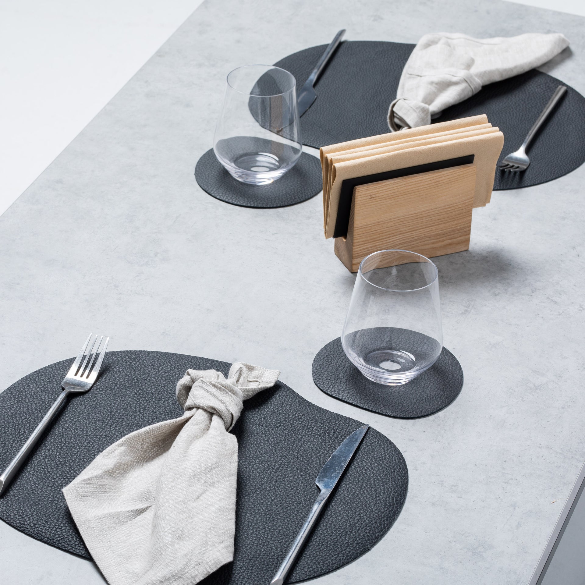 Black leather placemat and coaster on a modern dining table setting with utensils.
