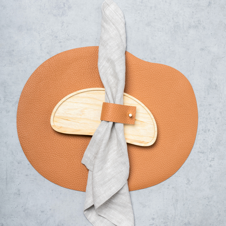 Leather napkin ring mustard with wood detail holding a gray linen napkin on a textured background.