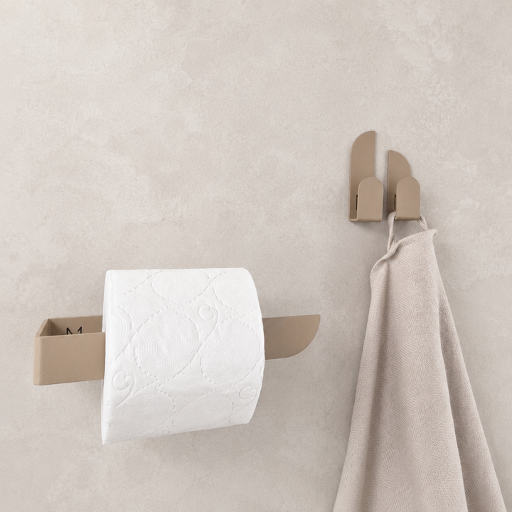 Adhesive beige toilet paper holder mounted on a wall with paper towels and a hand towel.