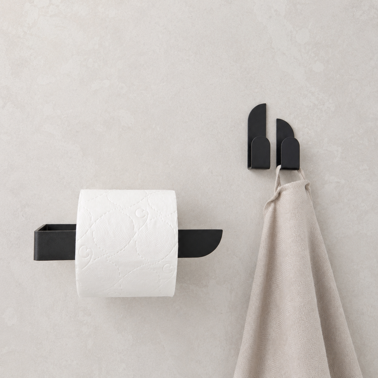 Adhesive black toilet paper holder mounted on a wall with a roll of toilet paper and a towel hanging beside it.