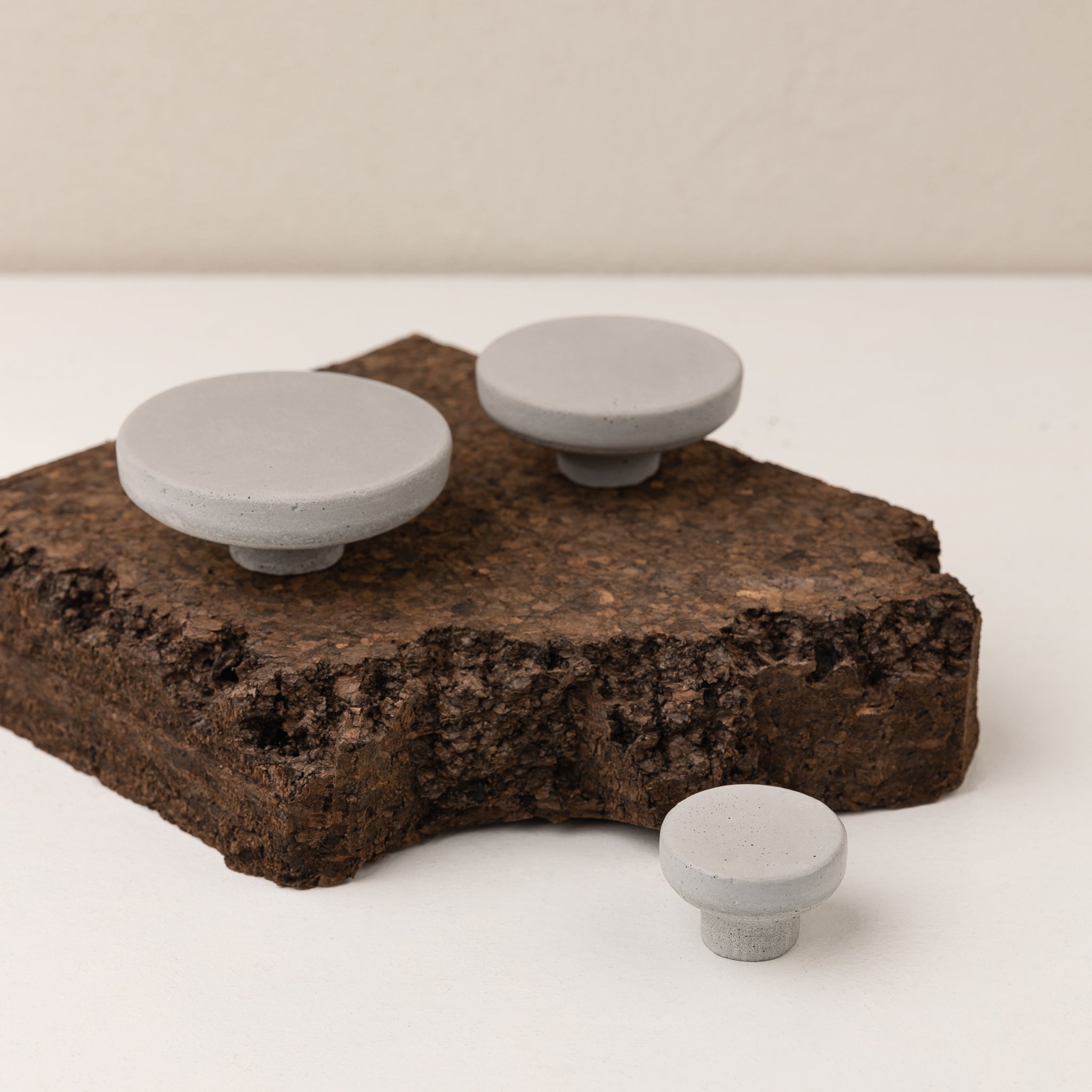 Light grey concrete wall hook set displayed on a natural cork surface, showcasing handmade craftsmanship.