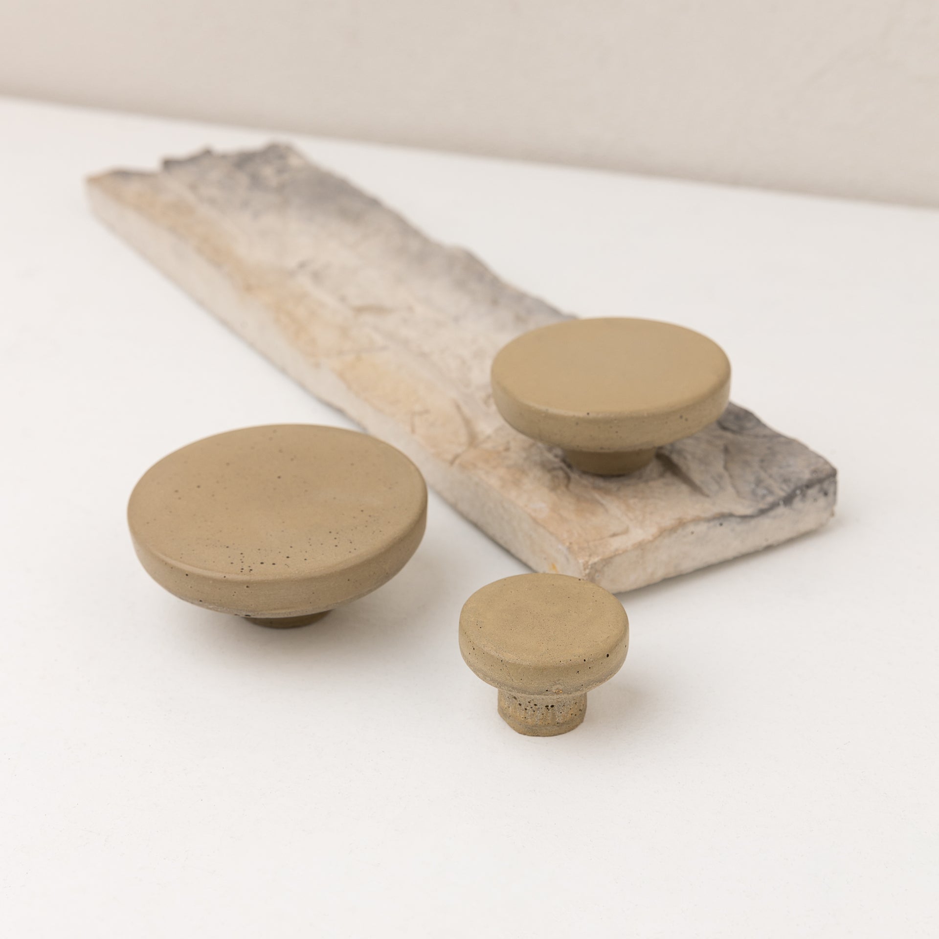 Concrete wall hook beige POMOLO displayed on a natural wooden surface in three varying sizes.