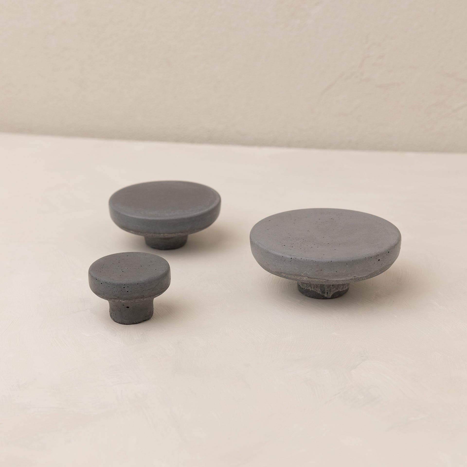 Concrete wall hook dark grey POMOLO set of three handmade knobs on a light surface.