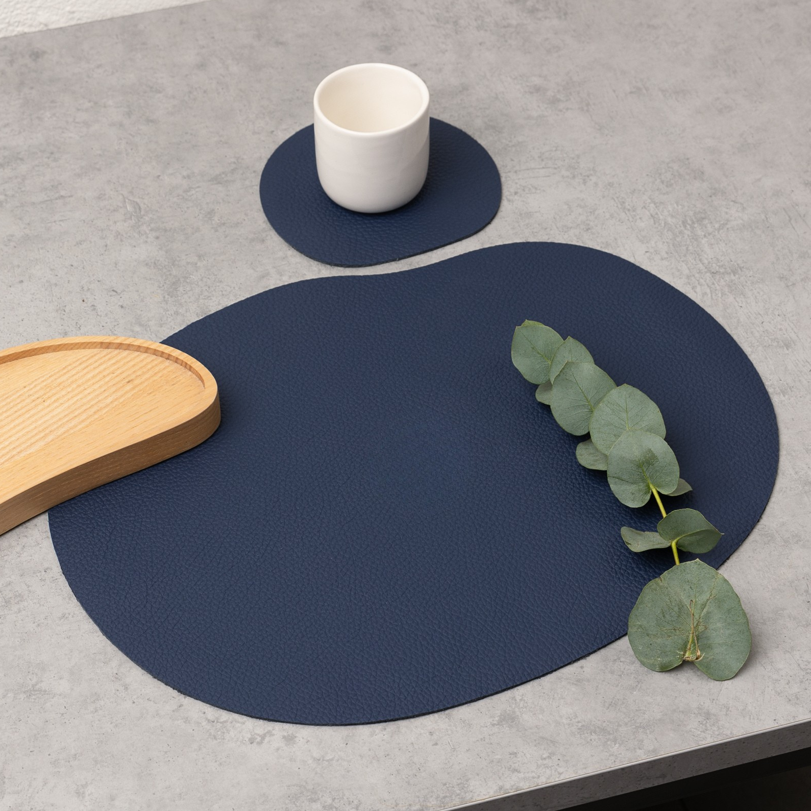 Dark blue leather placemat and coaster on a table with a cup and eucalyptus, ideal for elegant dining.