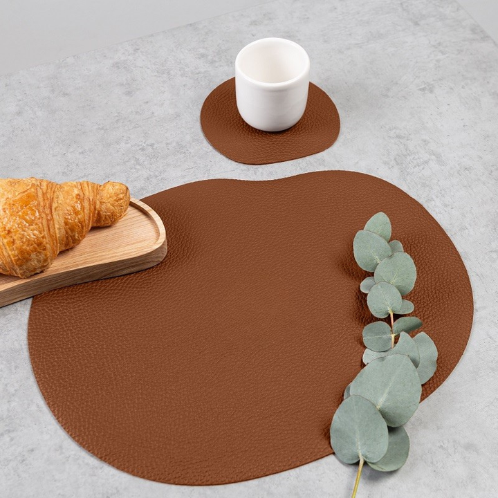 Terracotta Leather placemat and coaster arrangement with a croissant and cup on a modern table.