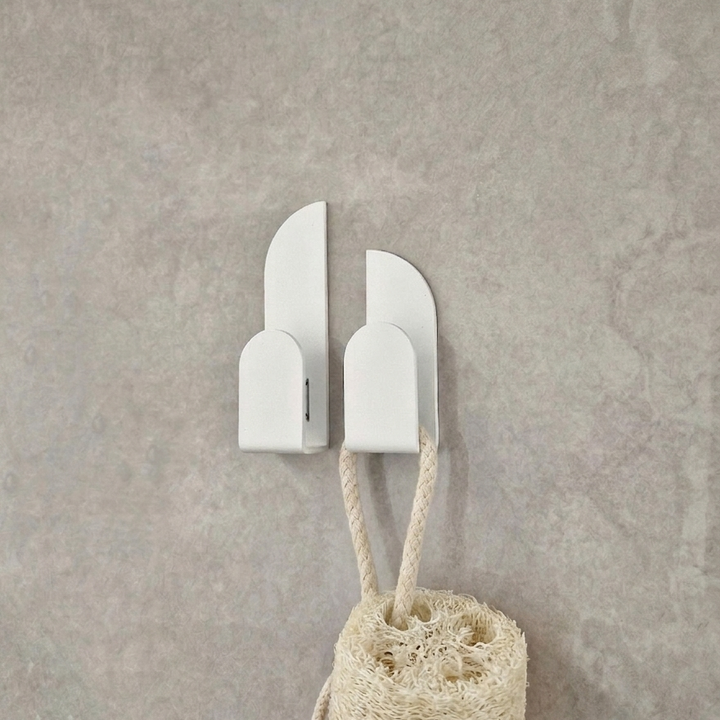Adhesive wall hooks BAUHAUS mounted on a wall holding a loofah in a minimalist design.