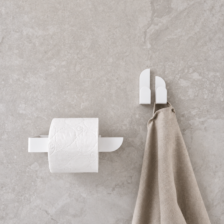 Modern adhesive white toilet paper holder mounted on a grey wall with a towel.